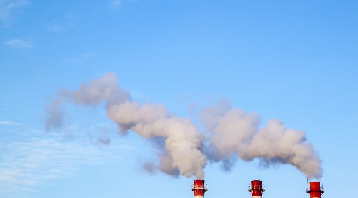 Smoking industrial stacks in a thermal power plant emit polluted air into the atmosphere in the blue sky