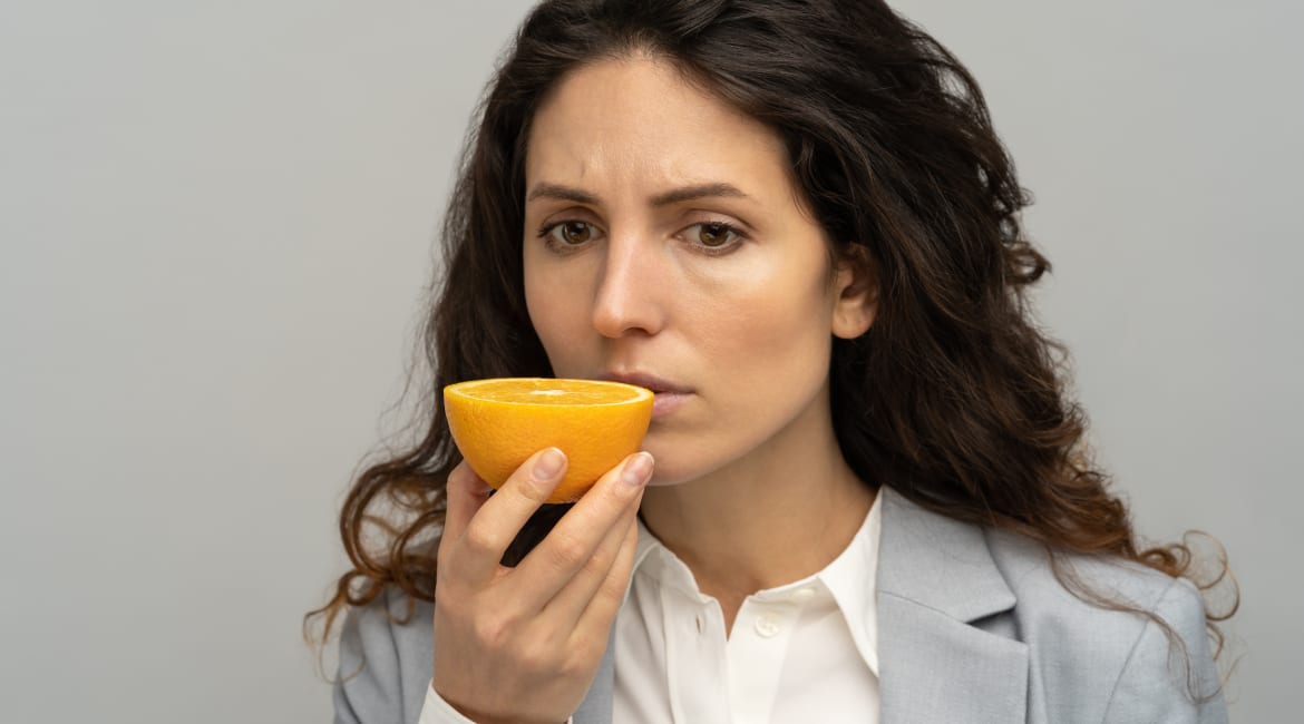 Sick business woman trying to sense smell of half fresh orange, has symptoms of Covid-19.