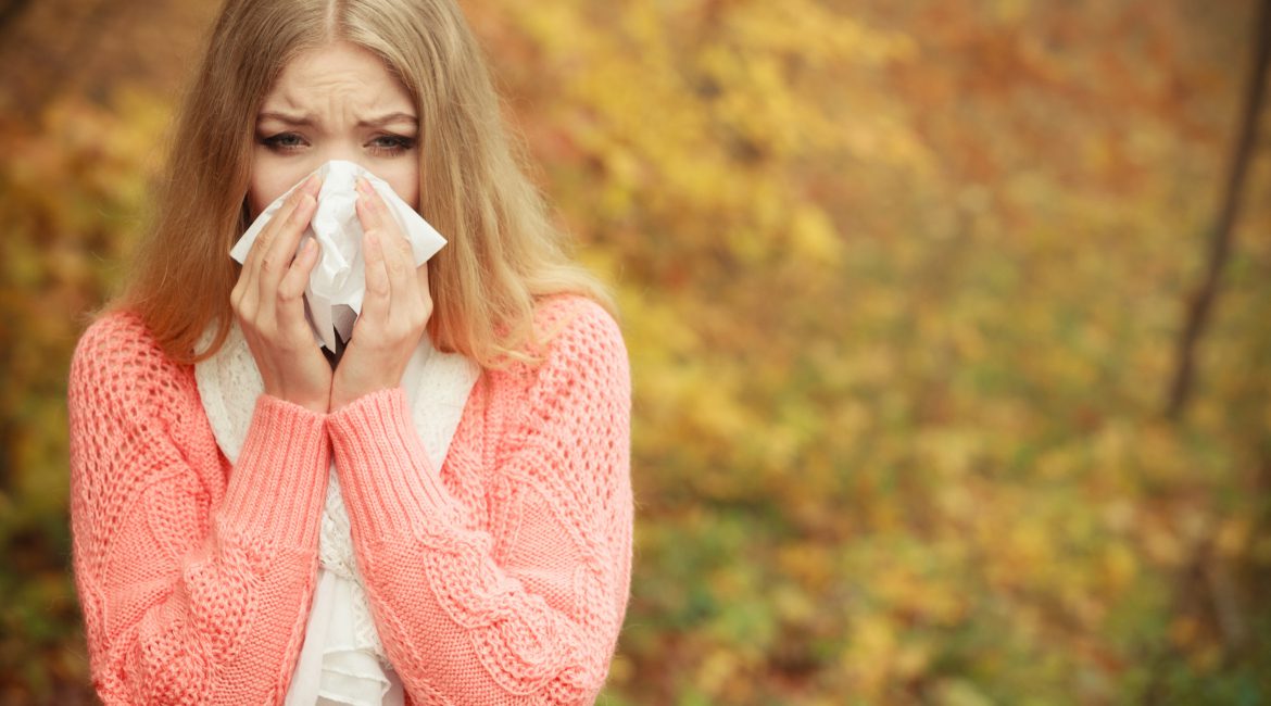 Sick ill woman in autumn park sneezing in tissue.