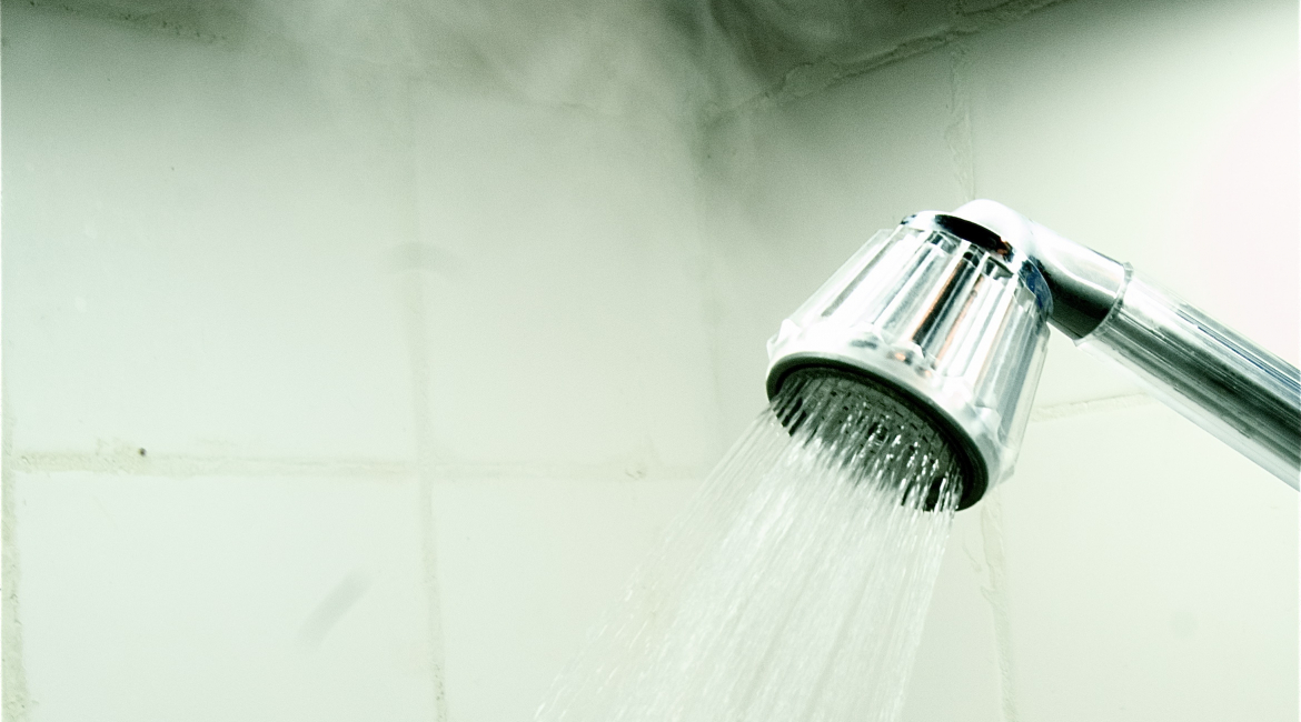 Close-Up Of Flowing Water From Shower Faucet With Steam In Bathr
